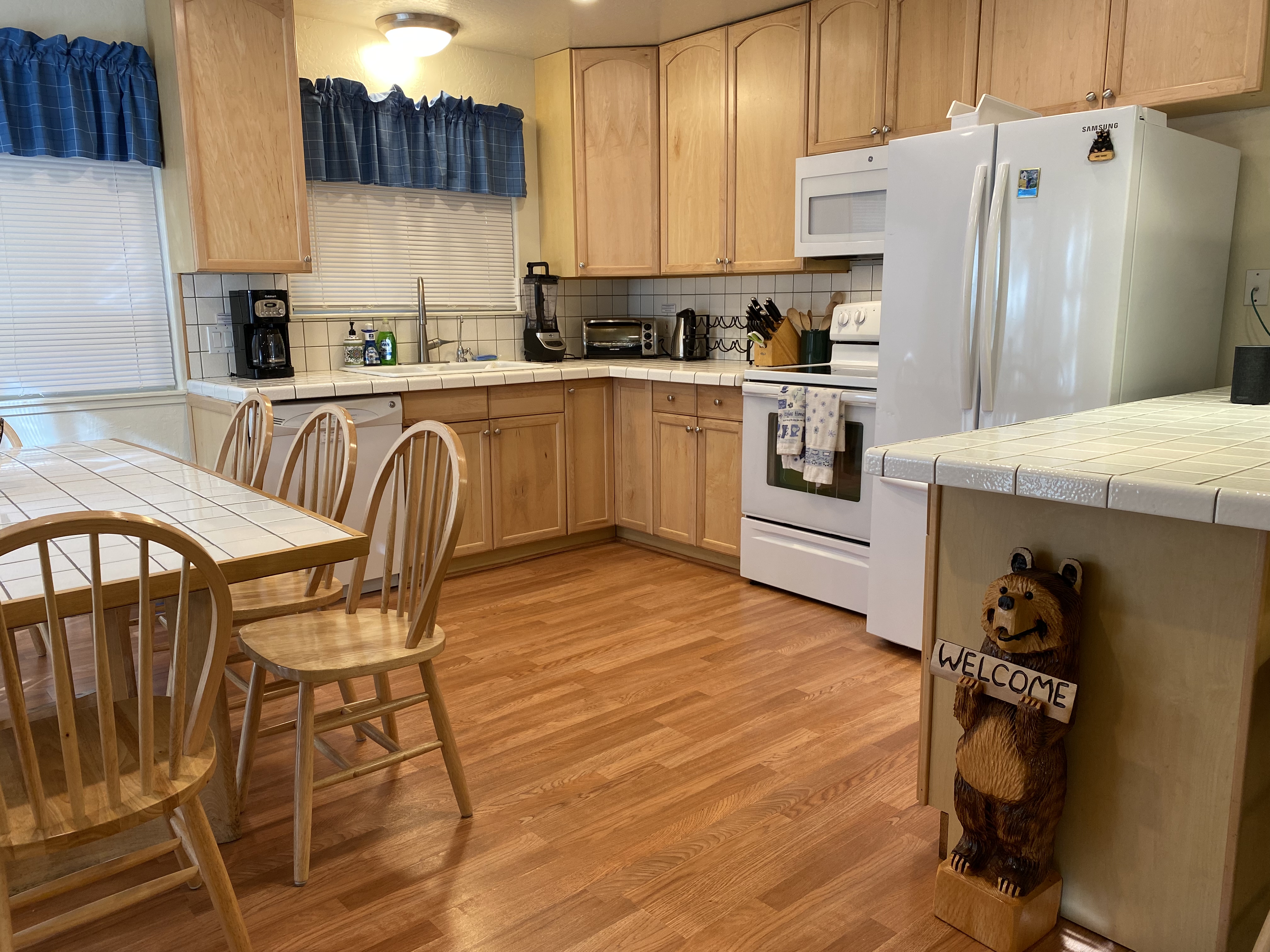 Kitchen with carved welcome bear, wood cabinets, white tile counters, and dining table