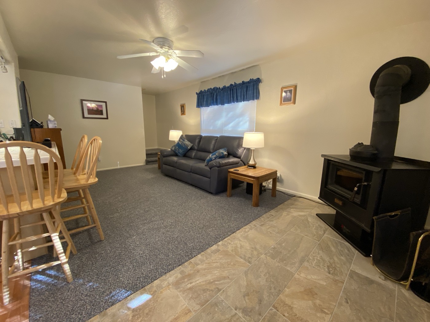 Living room from the breakfast bar with grey leather couch, wood stove, and blue valance